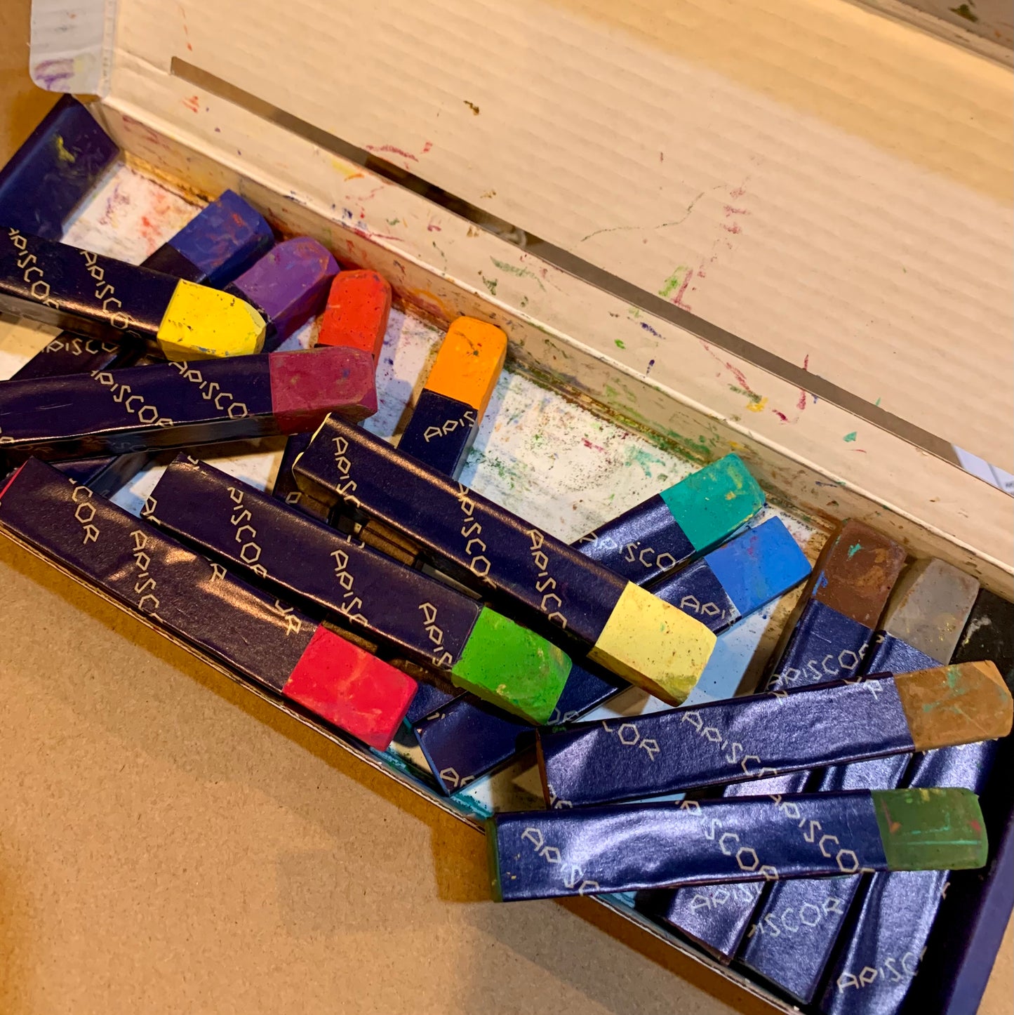An open box of Apiscor 's colourful chalks on a teachers desk.