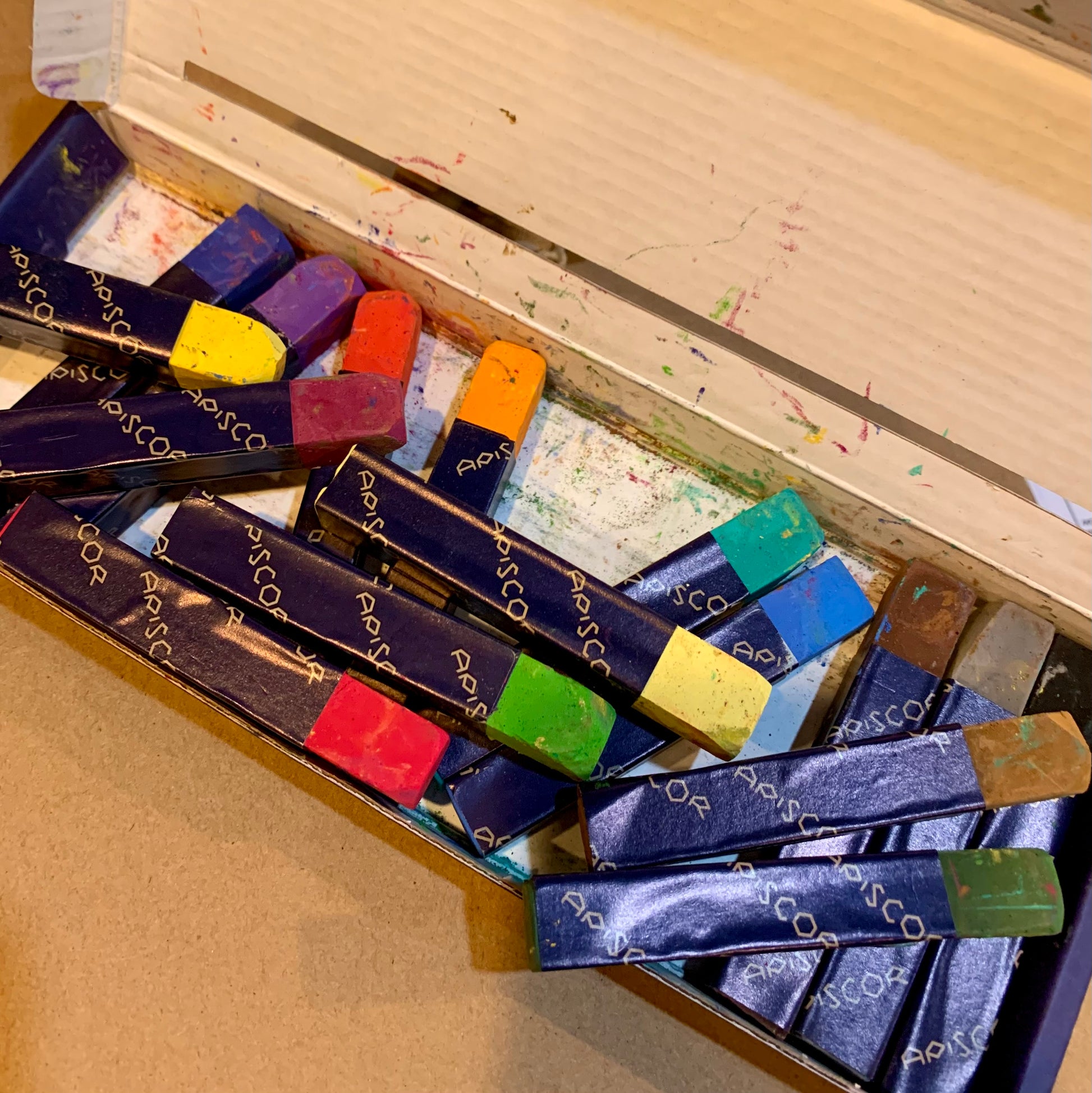 An open box of Apiscor 's colourful chalks on a teachers desk.