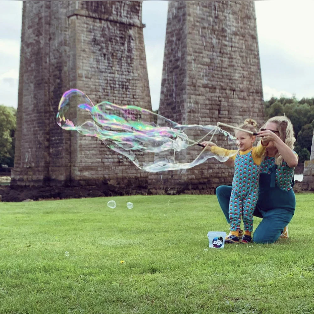 A woman helping a small child to make giant bubbles in a park