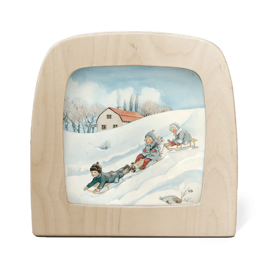 A wooden silhouette screen featuring three children having fun on tobogans in the snow