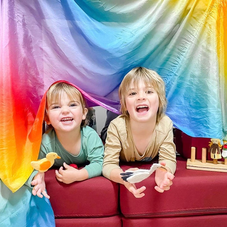 Two children playing puppet shows  behind a colorful rainbow silk fabric backdrop