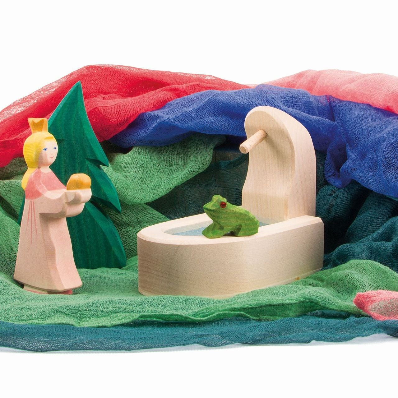 Wooden play set with frog prince and princess, well, and on a selection of colorful cotton muslin fabric background scenery