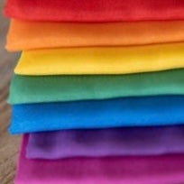 a stack of folded colourful silks in rainbow order from pink at the bottom, purple, blue, green, yellow, orange, and red on top