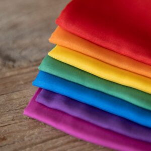 Stack of colorful play silks on a wooden surface