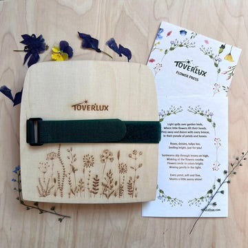 Toverlux flower press product with a velcro strap on a wooden surface with flowers and information flyer.