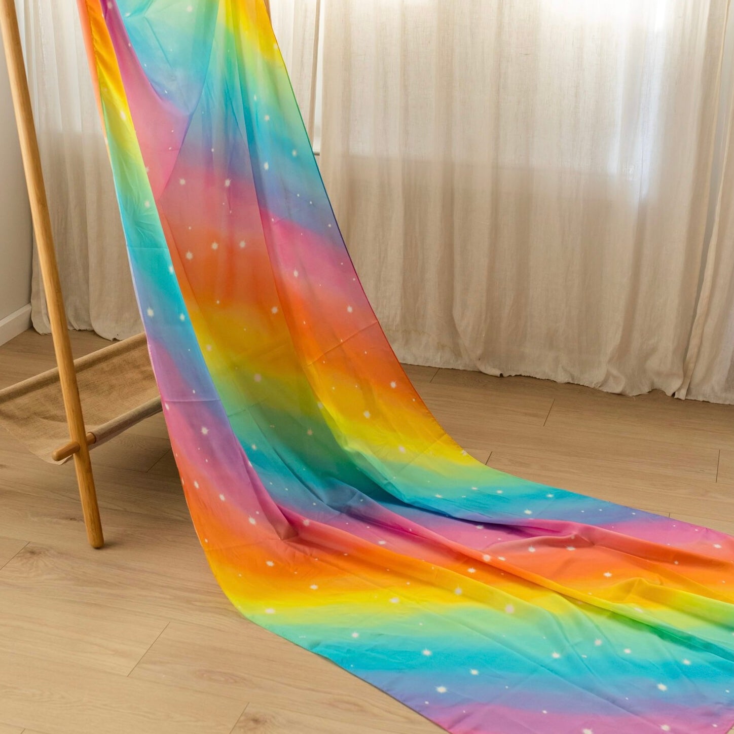Colorful rainbow-patterned exra large silk fabric draped over a wooden frame on a light wooden floor.