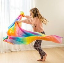 girl dancing with a colorful rainbow silk scarf in a room with white curtains.