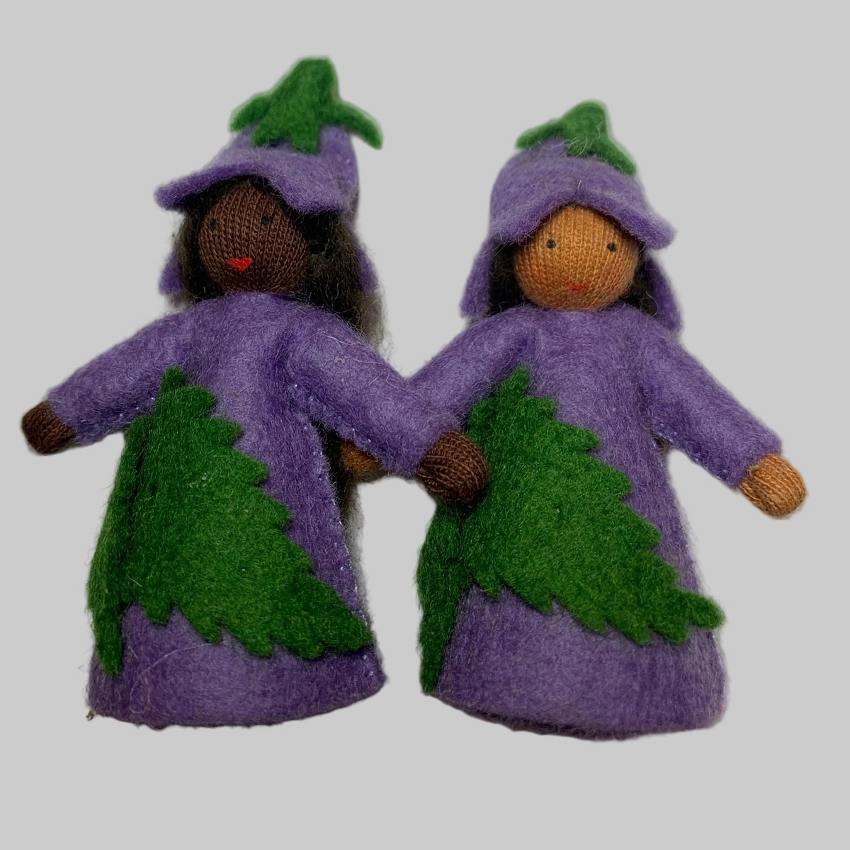 Two small handmade felt bluebell dolls dressed in purple and green outfits, standing side by side on a plain white surface.