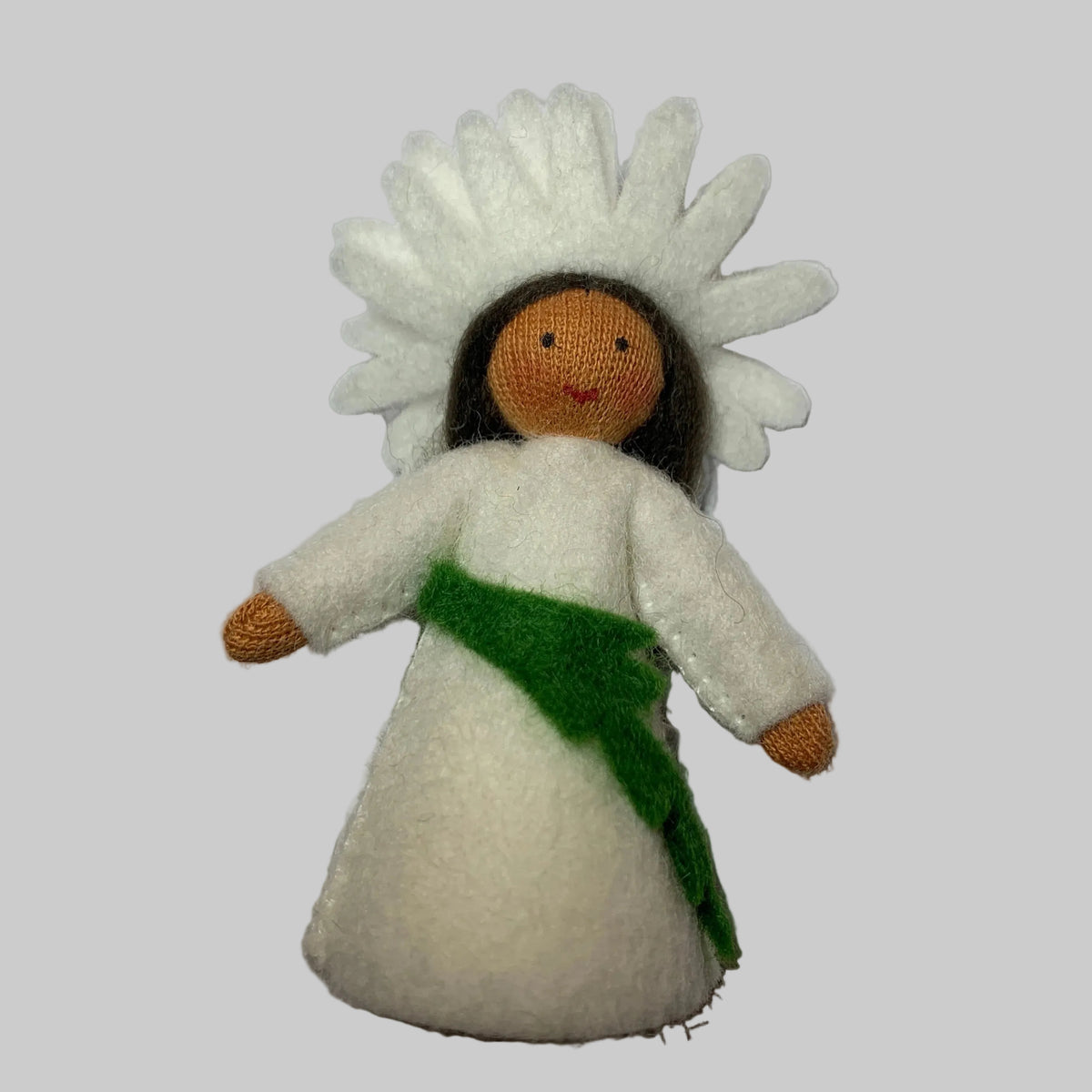 A small handmade felt daisy doll with a white dress, green sash, brown face and hands, and a white flower headdress, photographed on a plain white background