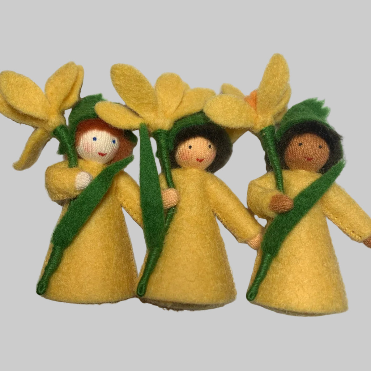 Three small handmade felt flower fairy dolls with yellow petals, green leaves, and simple embroidered faces, arranged on a white surface.