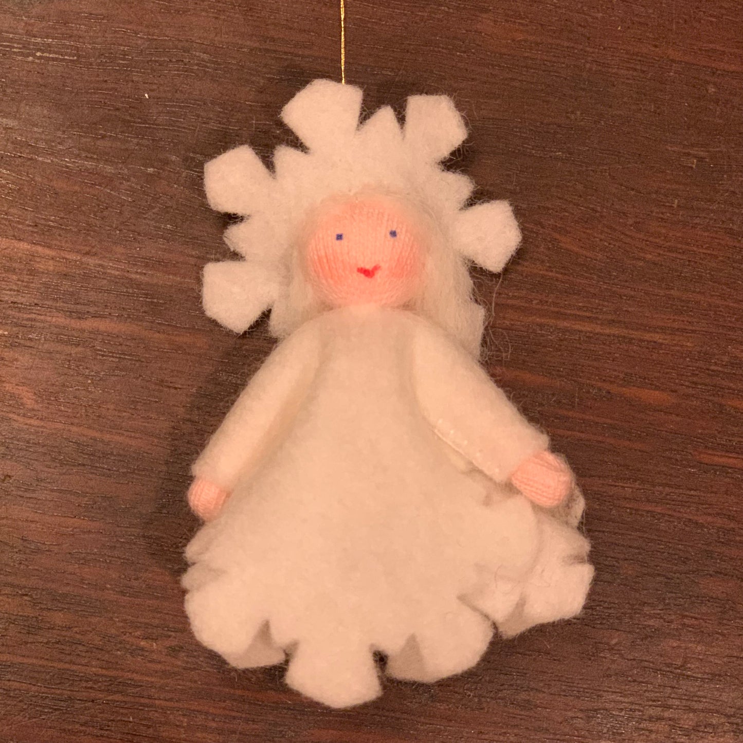 White snowflake angel ornament with a smiling face on a wooden surface