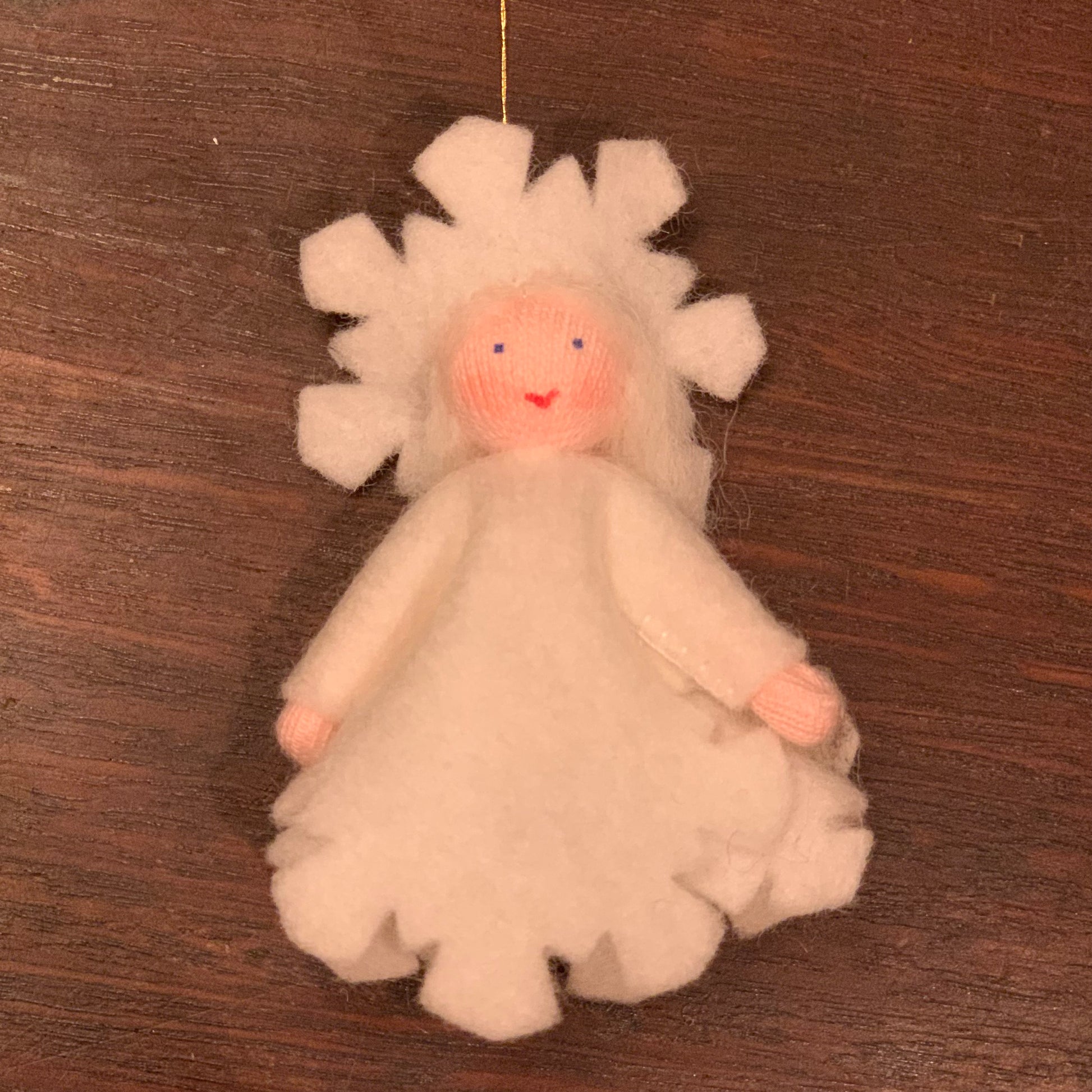 White snowflake angel ornament with a smiling face on a wooden surface