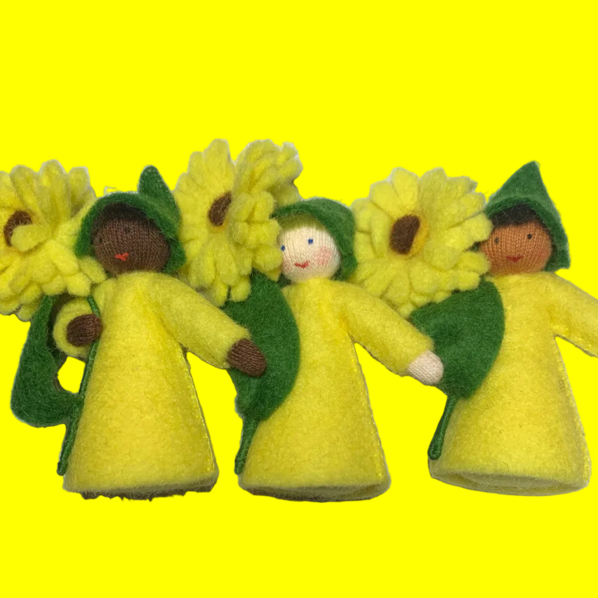 Three handmade felt calendula dolls wearing yellow and green outfits, arranged on a white surface.