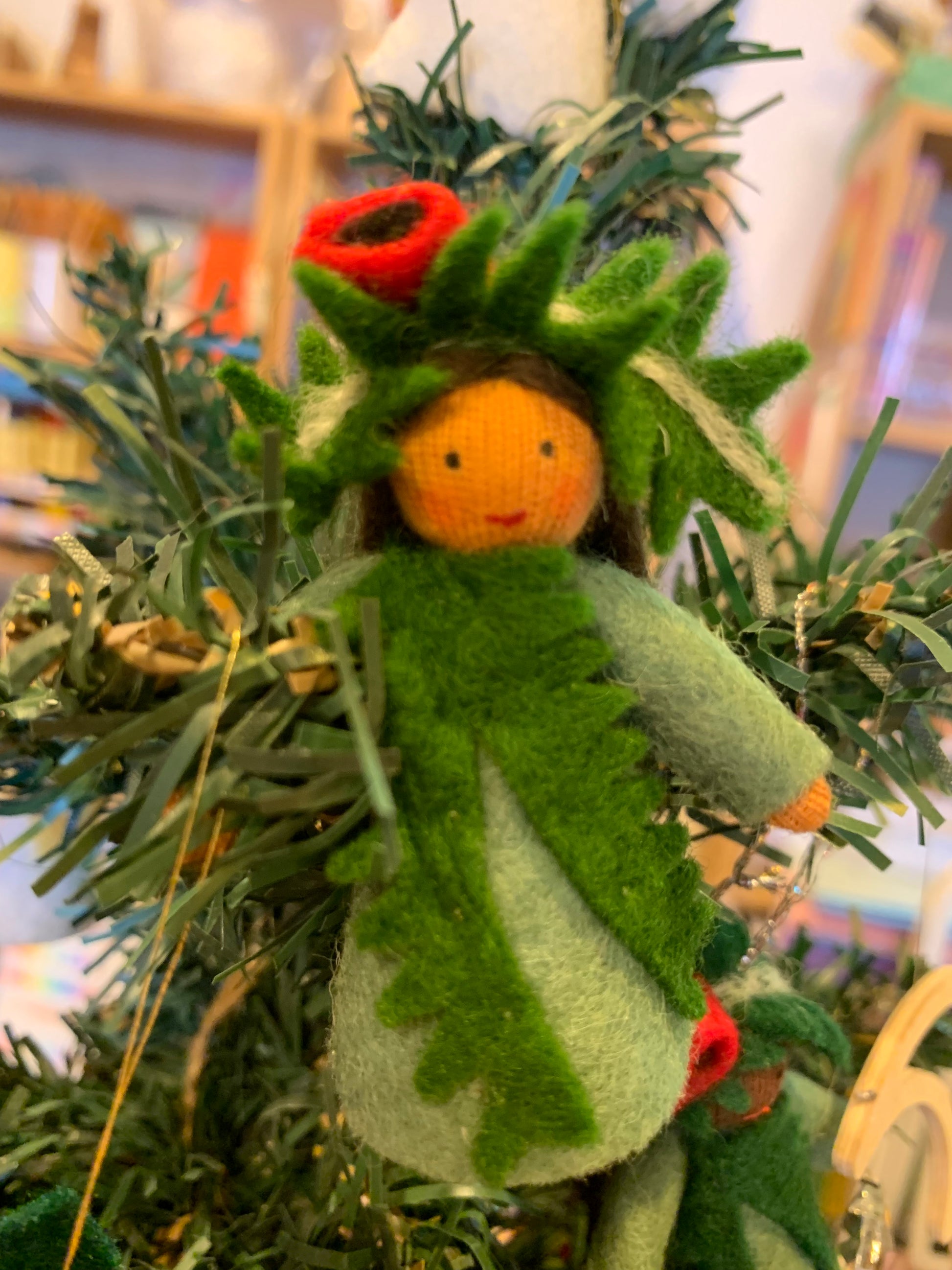 A felt craft Christmas ornament, a Yew tree fairy hanging in a Christmas tree, with a focus on red and green, representing the festive season.