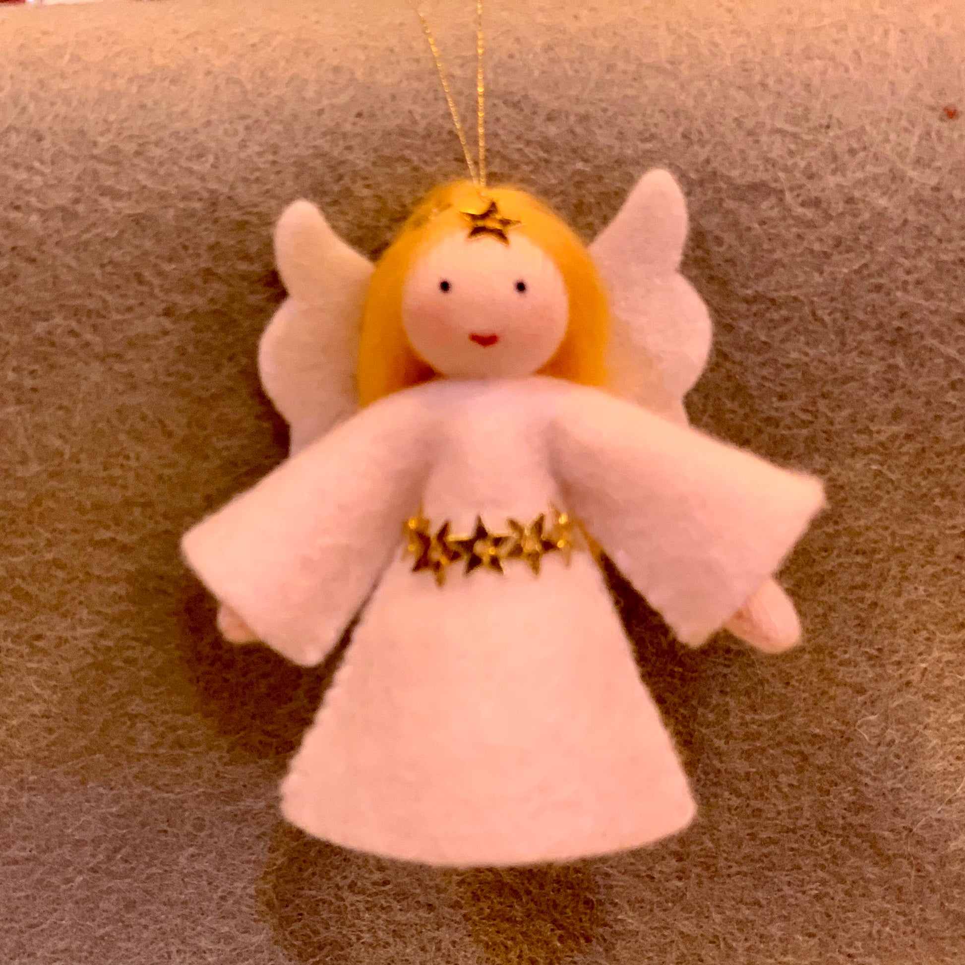 Decorative angel ornament with white dress, golden hair and gold sparkles on a textured surface
