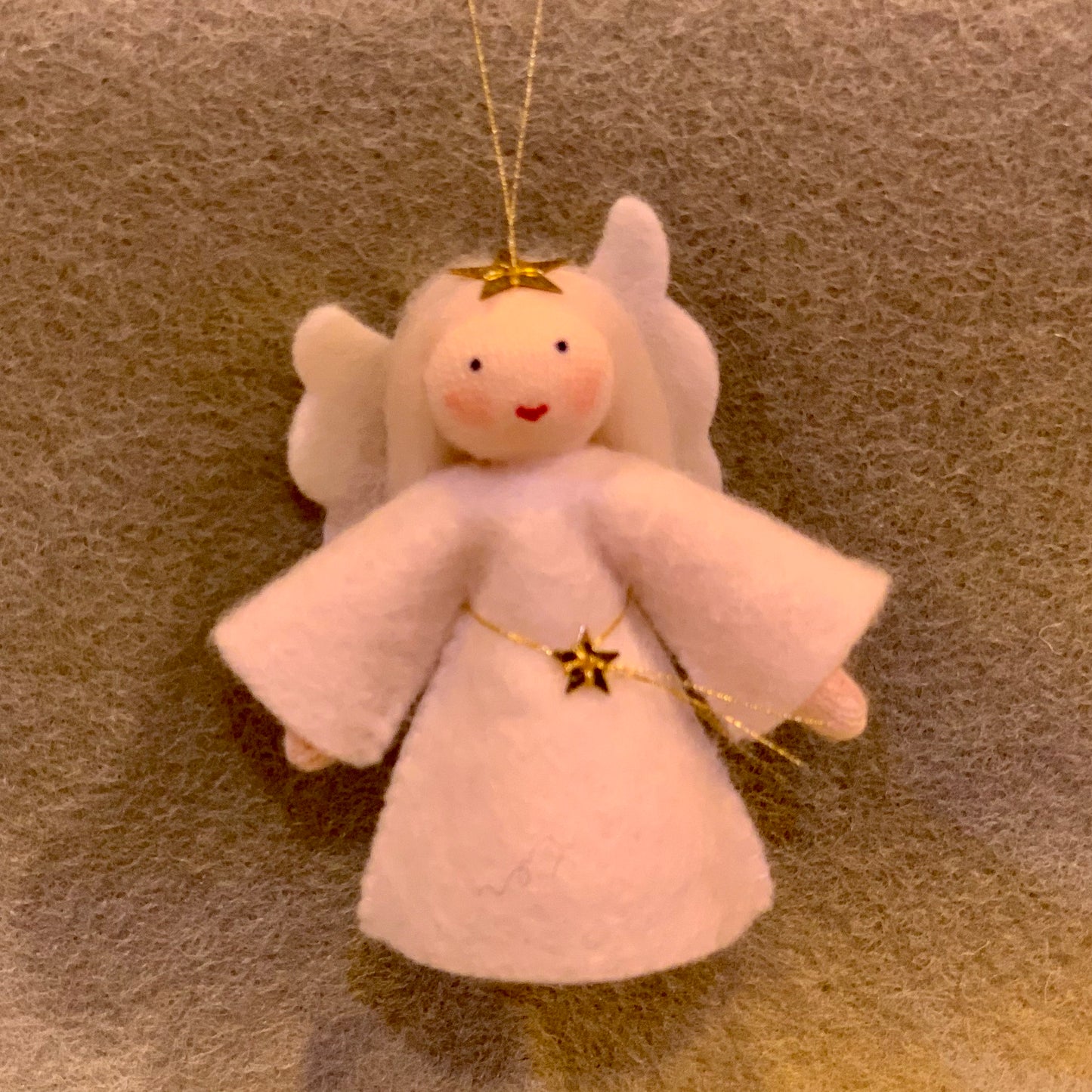 White angel ornament with white hairt and gold stars on a grey background