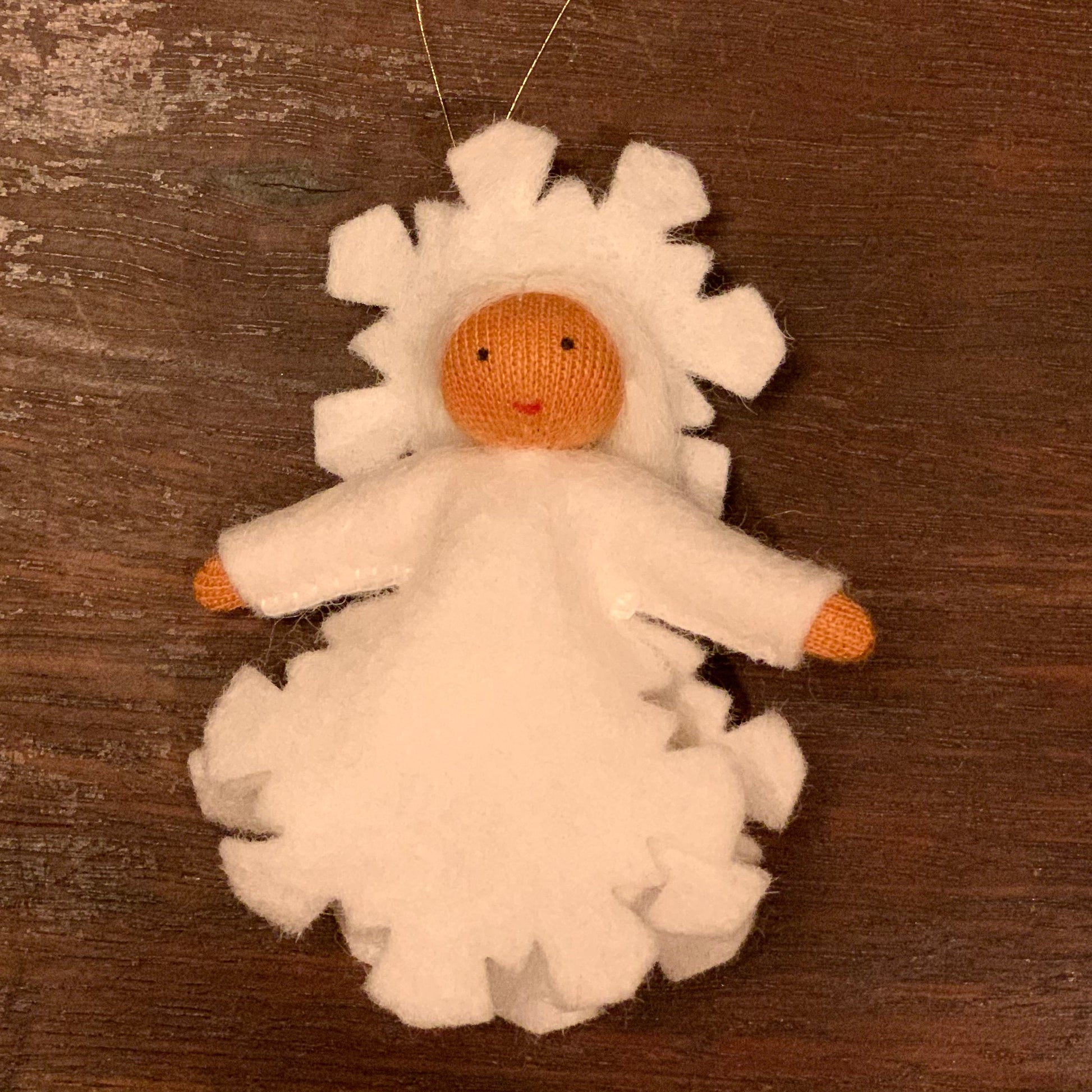 White felt angel ornament with white wings and medium skin tone on a wooden surface