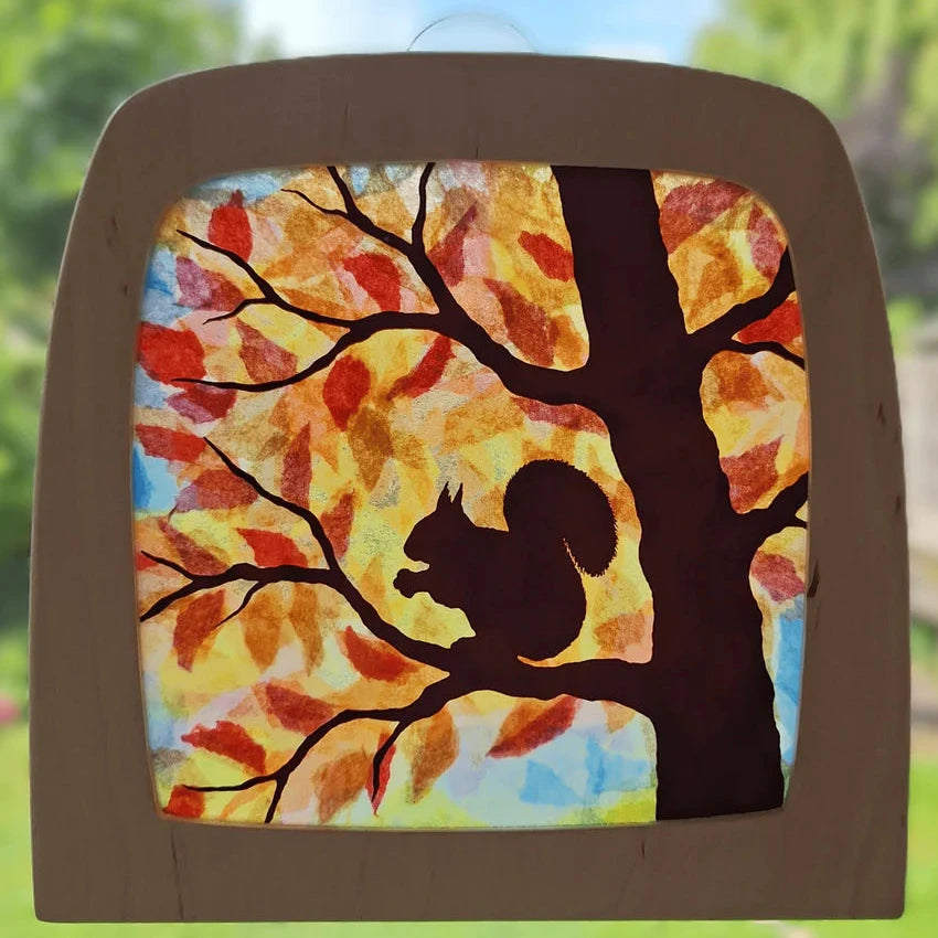 Window decoration with a squirrel on a tree branch against a colourful autumn leaf background.