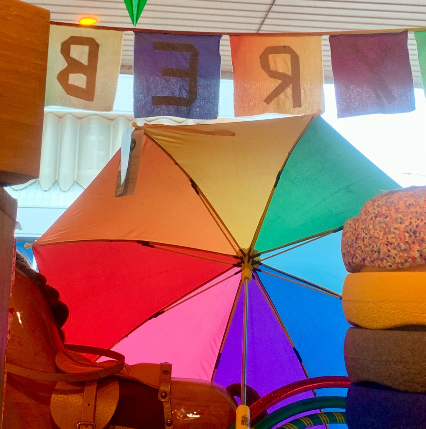 Colourful umbrella with rainbow panels , inside a window with a folded paper rainbow star on the glass 