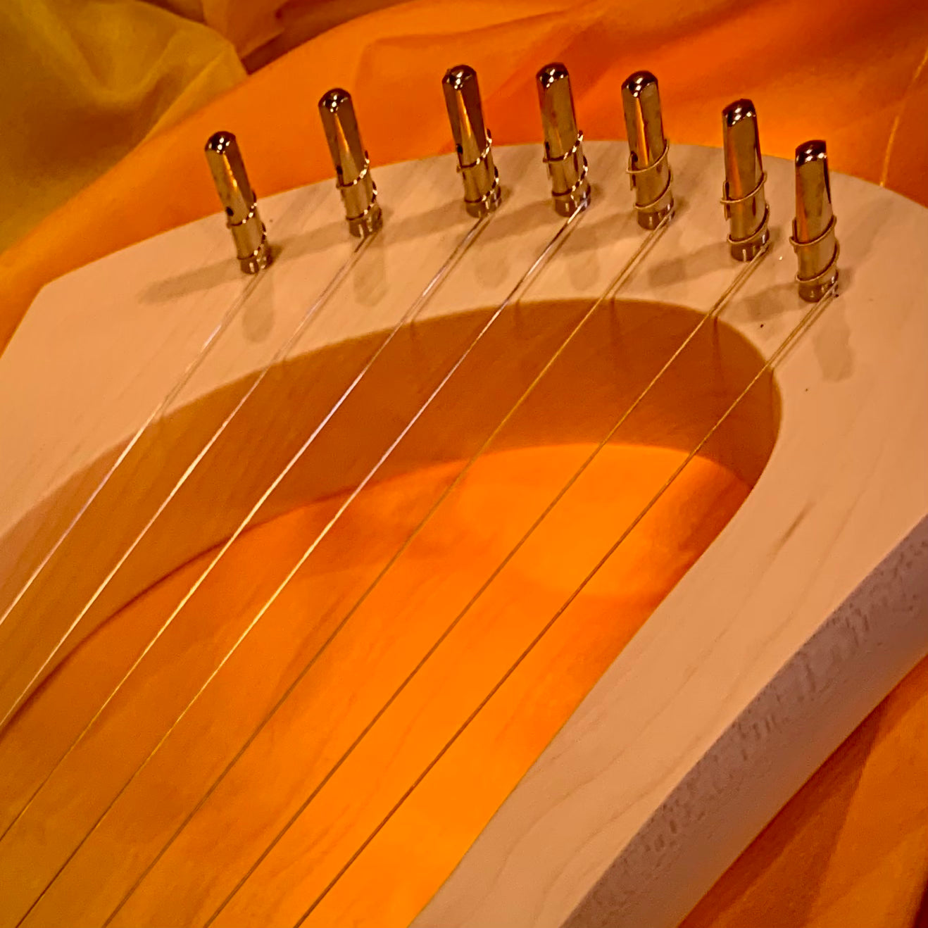 Showing the top tuning section of a small wooden lyre harp with seven pegs holding the fine wire strings 