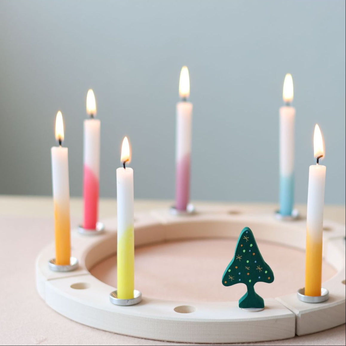 Wooden tree-shaped decoration on a white celebration ring with dip dye candles.