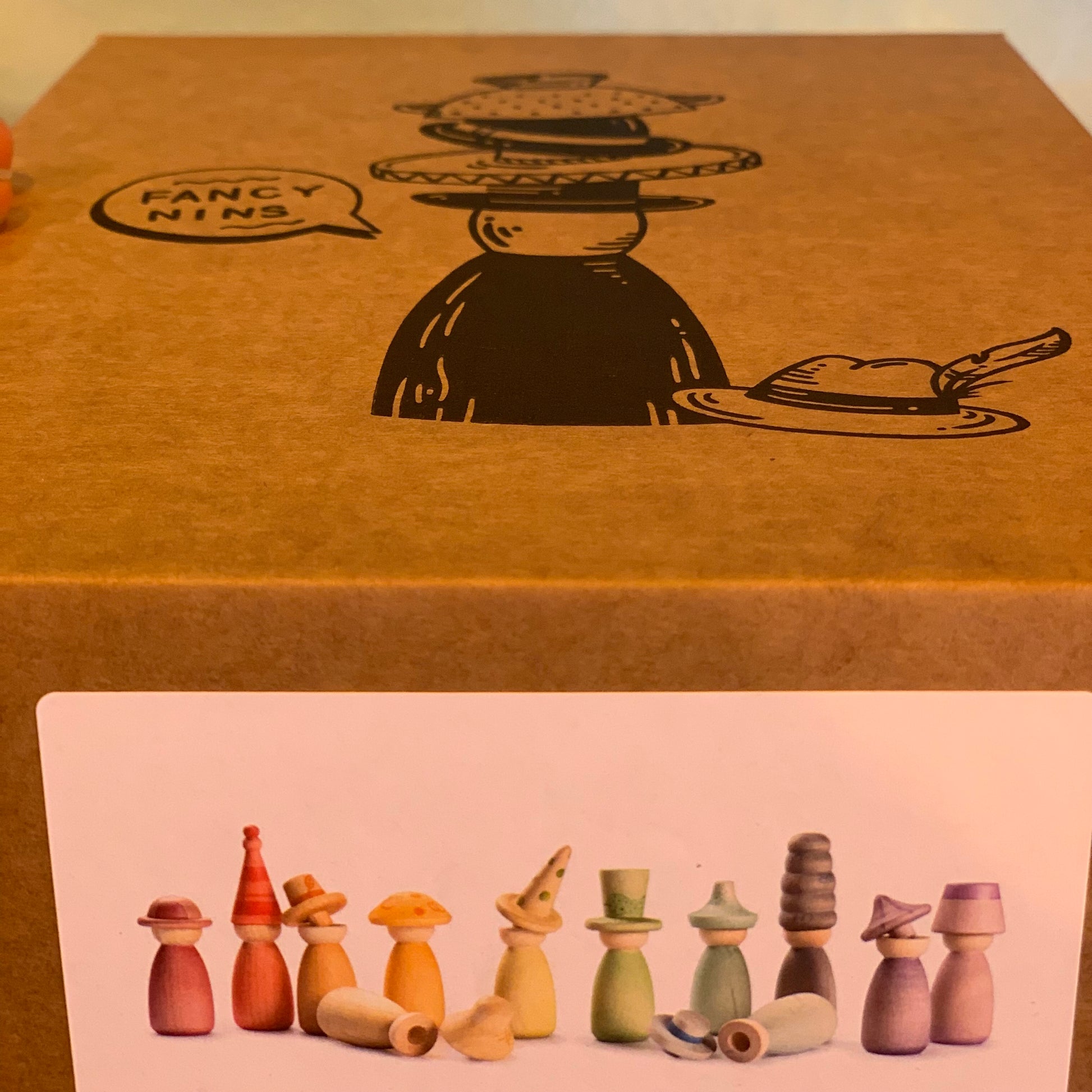Brown box with 'Fancy Nins' and illustrations of wooden peg dolls with removable hats.