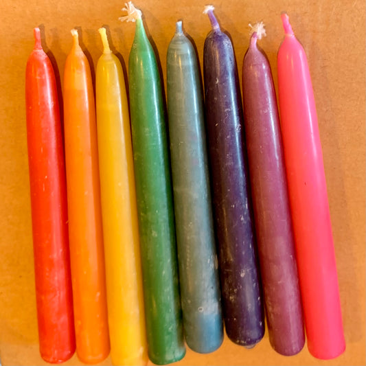 Row of colorful beeswax candles in rsinbowe order on a pink background