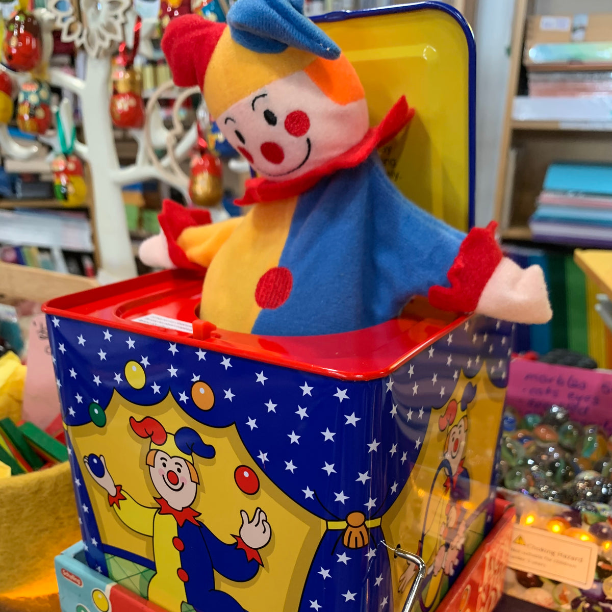Clown Jester toy in a tin box with colourful design, surrounded by books and toys.