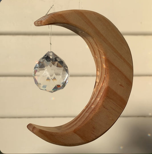 Wooden crescent moon ornament with a crystal hanging against a cream coloured wall