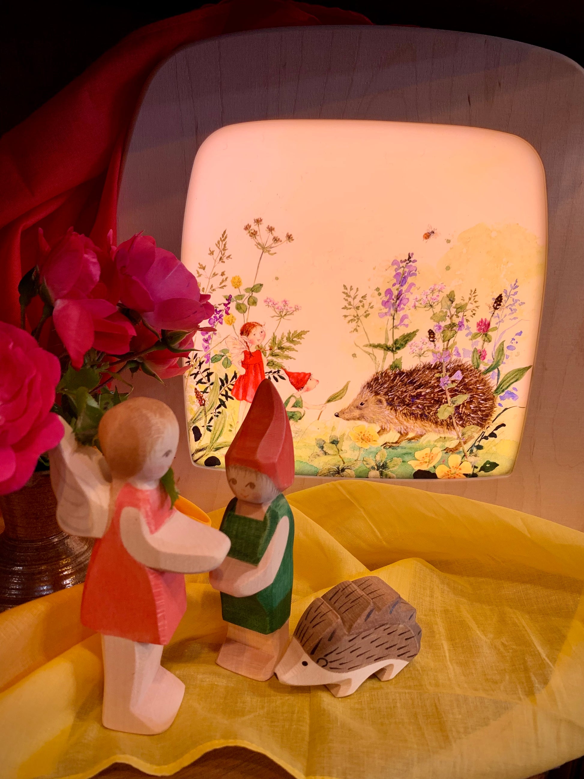 Decorative scene with fairy and elf and hedgehogs in front of a lamp depicting the same characters.