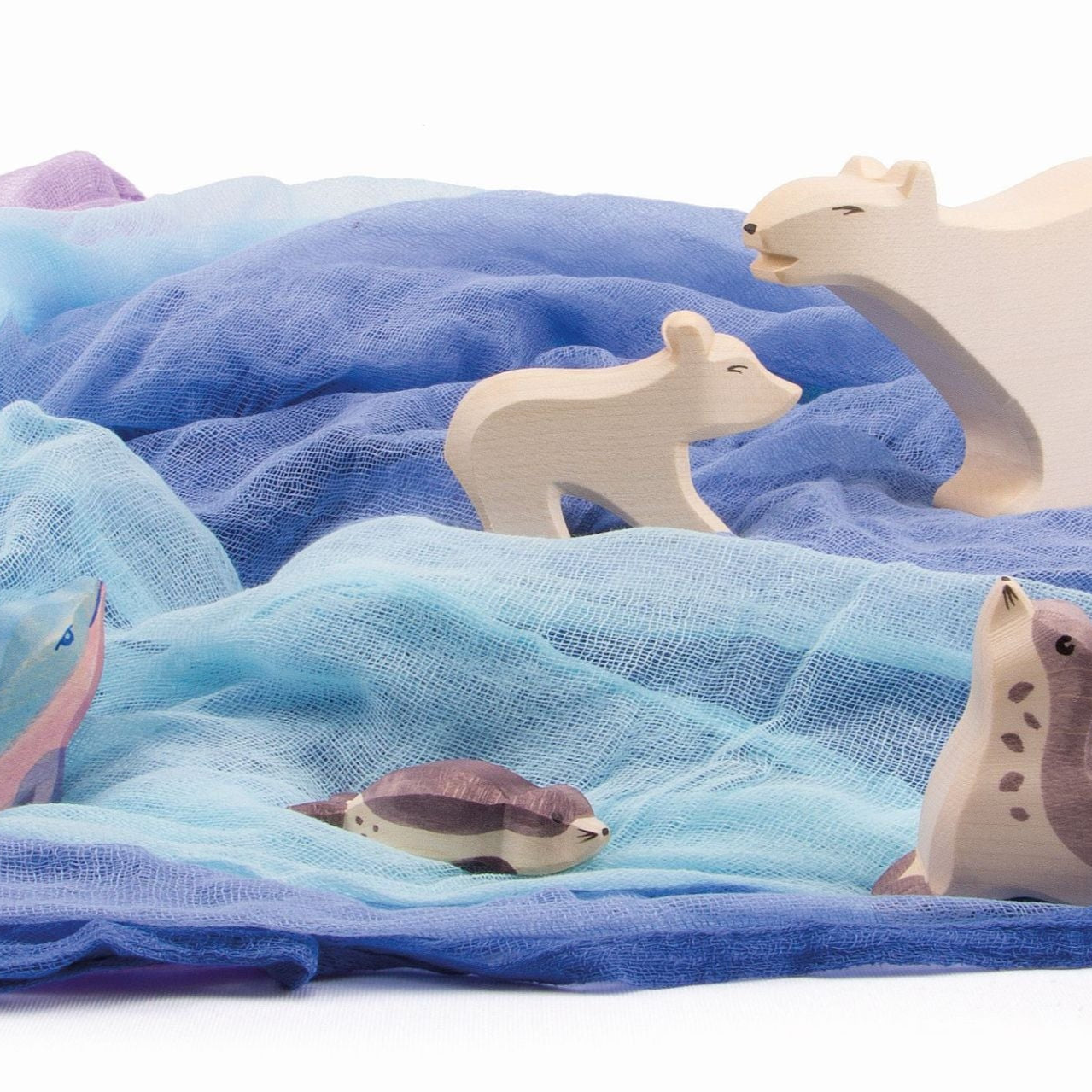Wooden polar bears, sea lions and dolphin toys on a backdrop of textured muslin cotton blue fabrics 