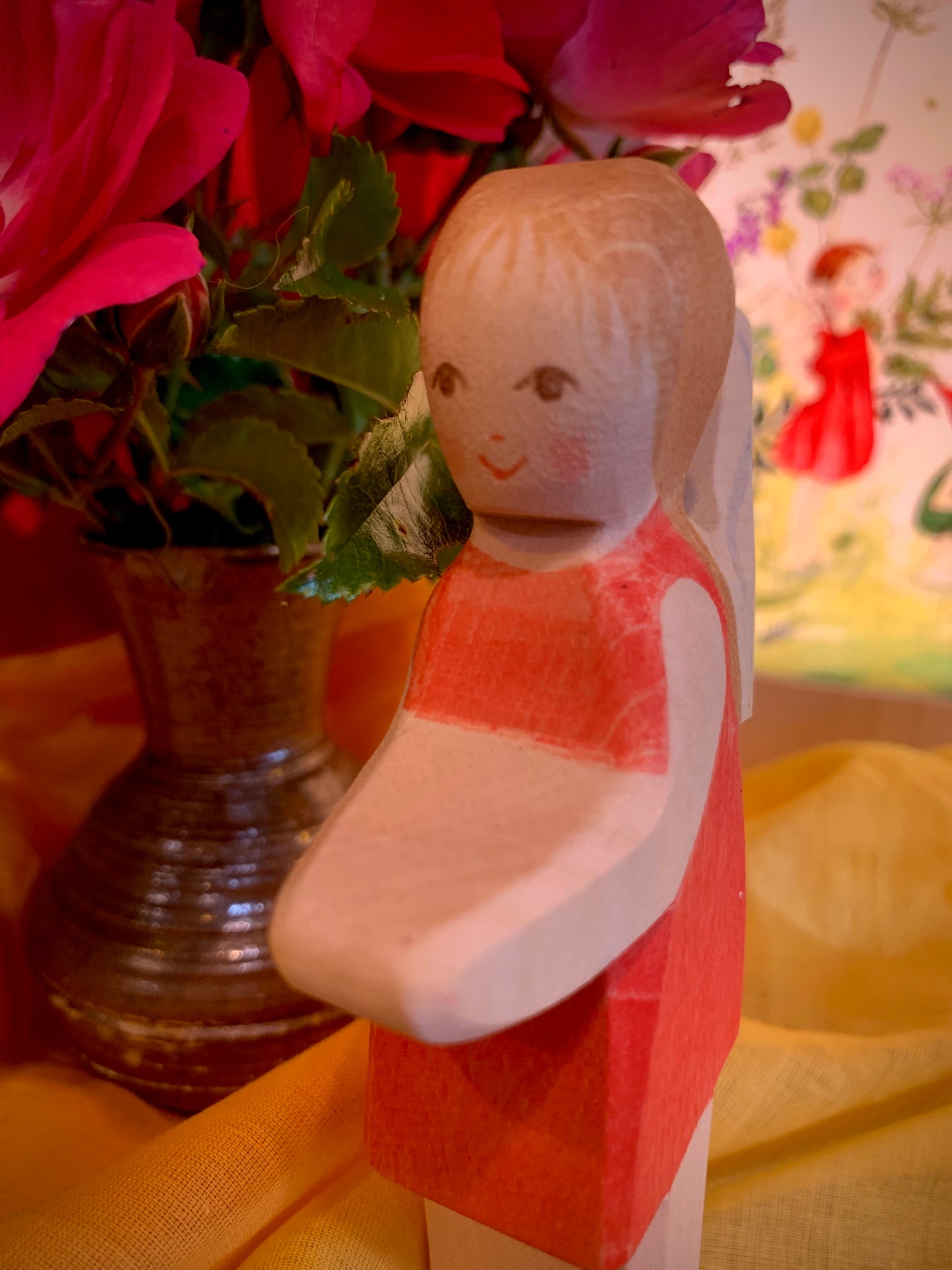 Wooden fairy doll with a red dress in front of pink flowers