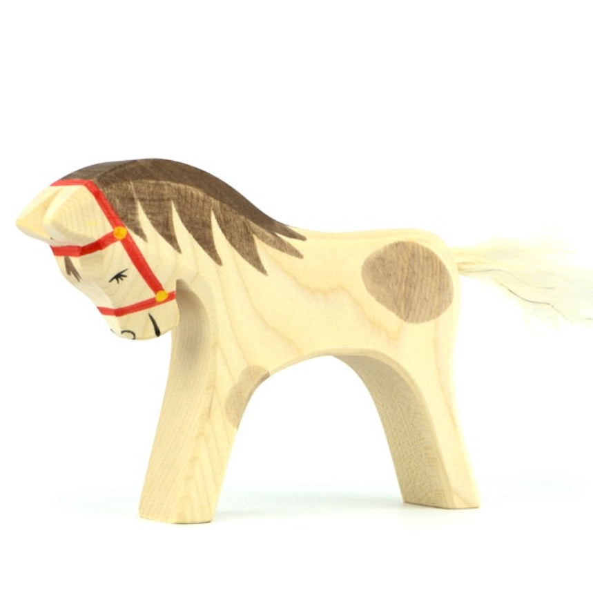 Wooden white spotted horse figurine with a red bridle on a white background