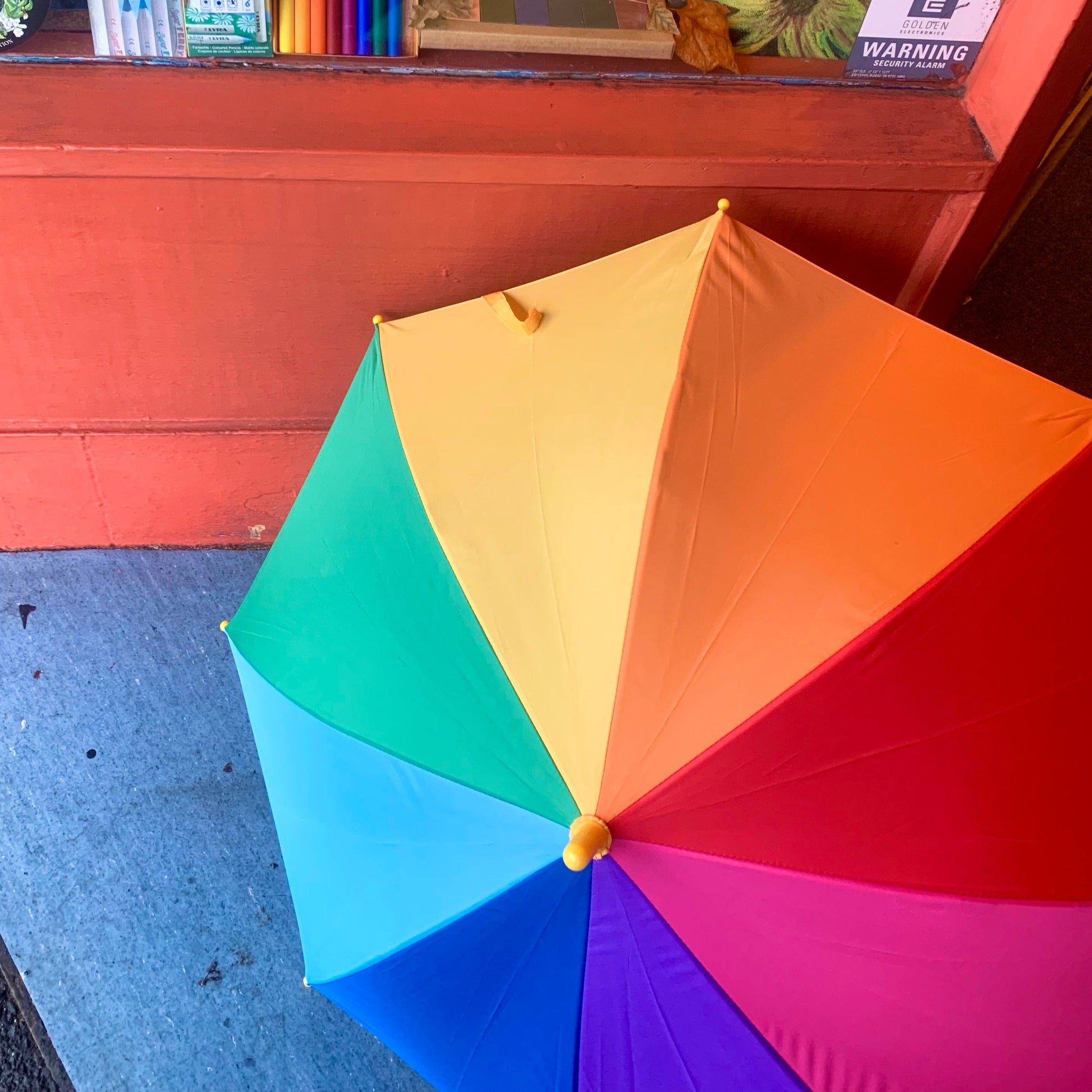 Colorful umbrella with a store shelf in the background displaying art supplies.