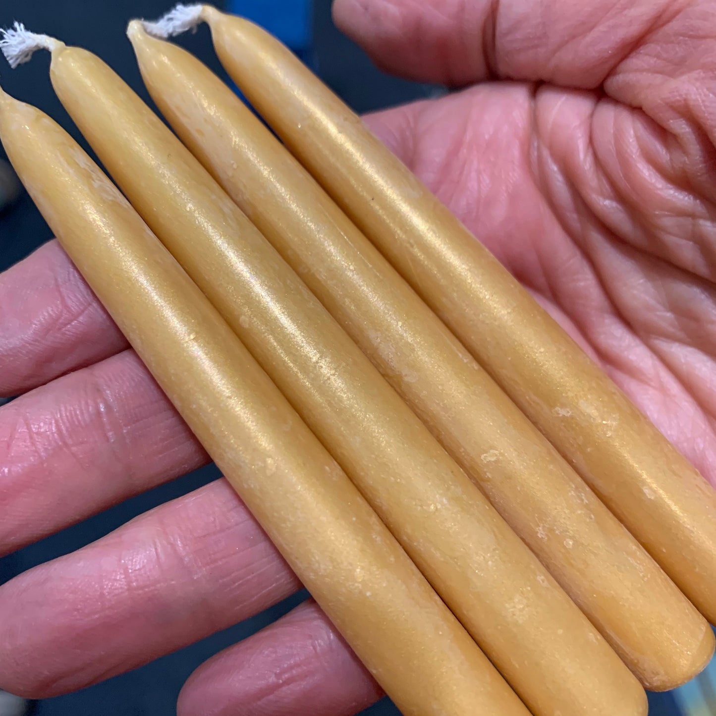 A set of four artisan beeswax candles, golden color, held in the palm of a hand