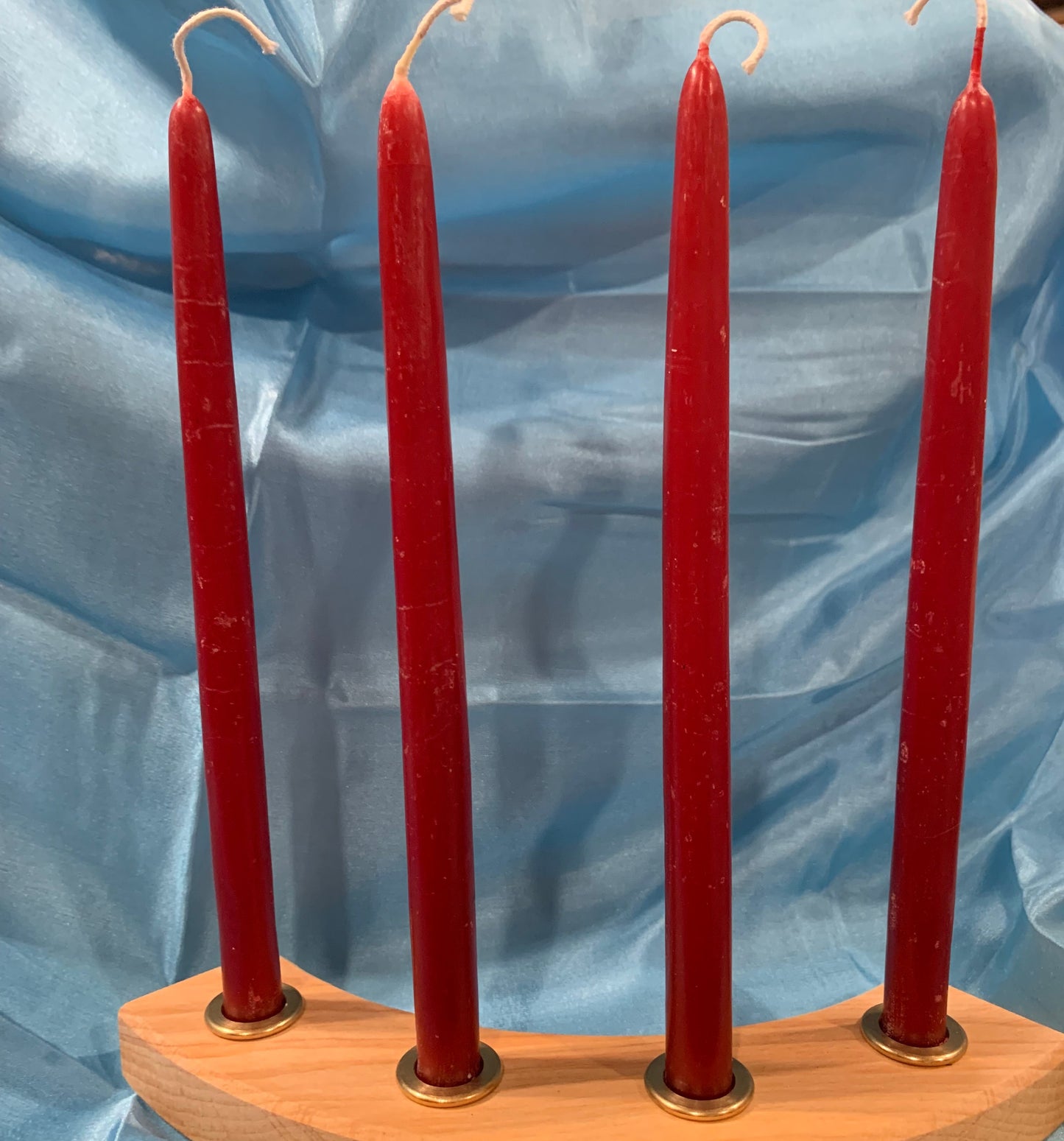 A set of four tall red artisan beeswax candles arranged in a wooden holder, in silk background.