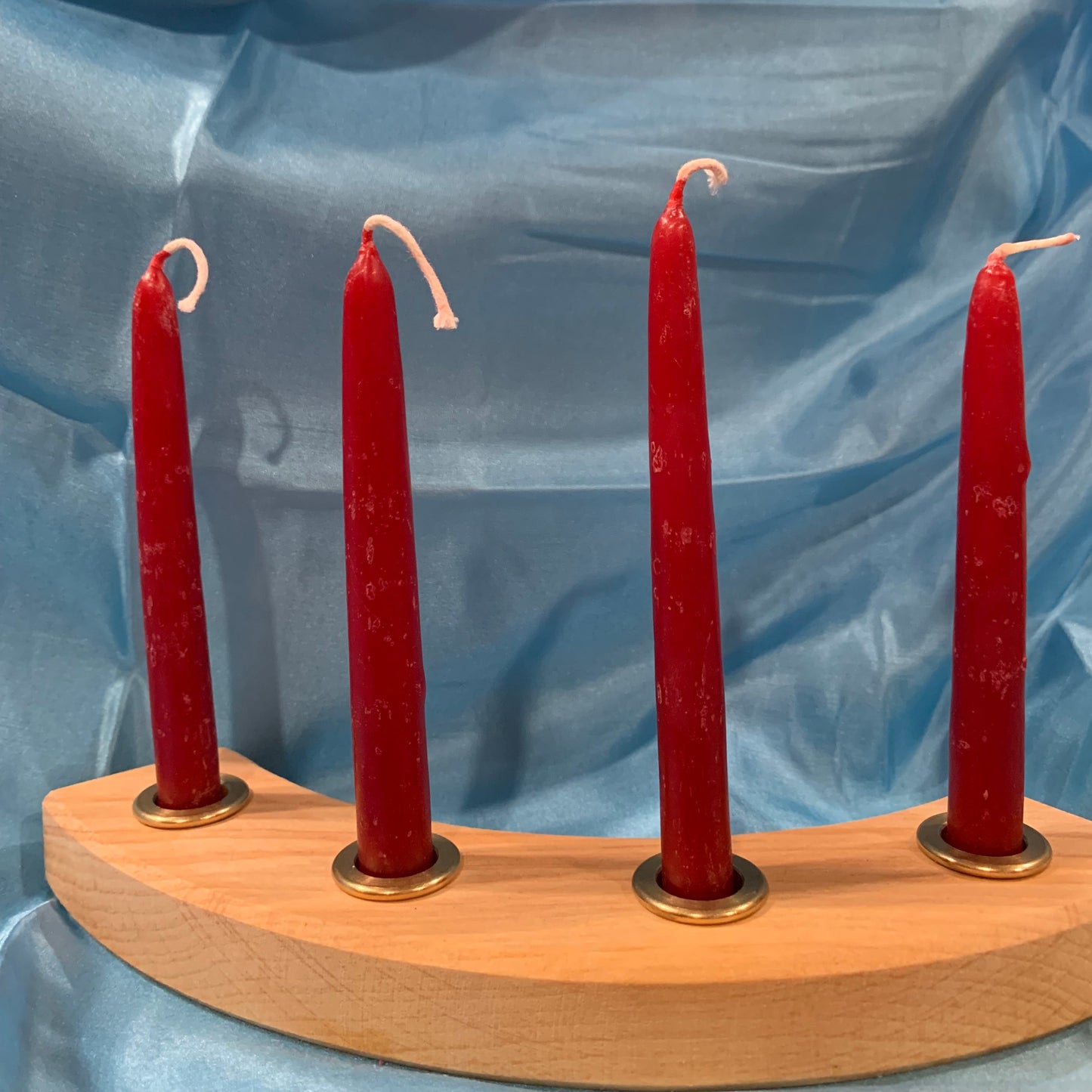 A set of four artisan beeswax candles arranged in a holder, hand dipped red color, displayed against a blue silk background.